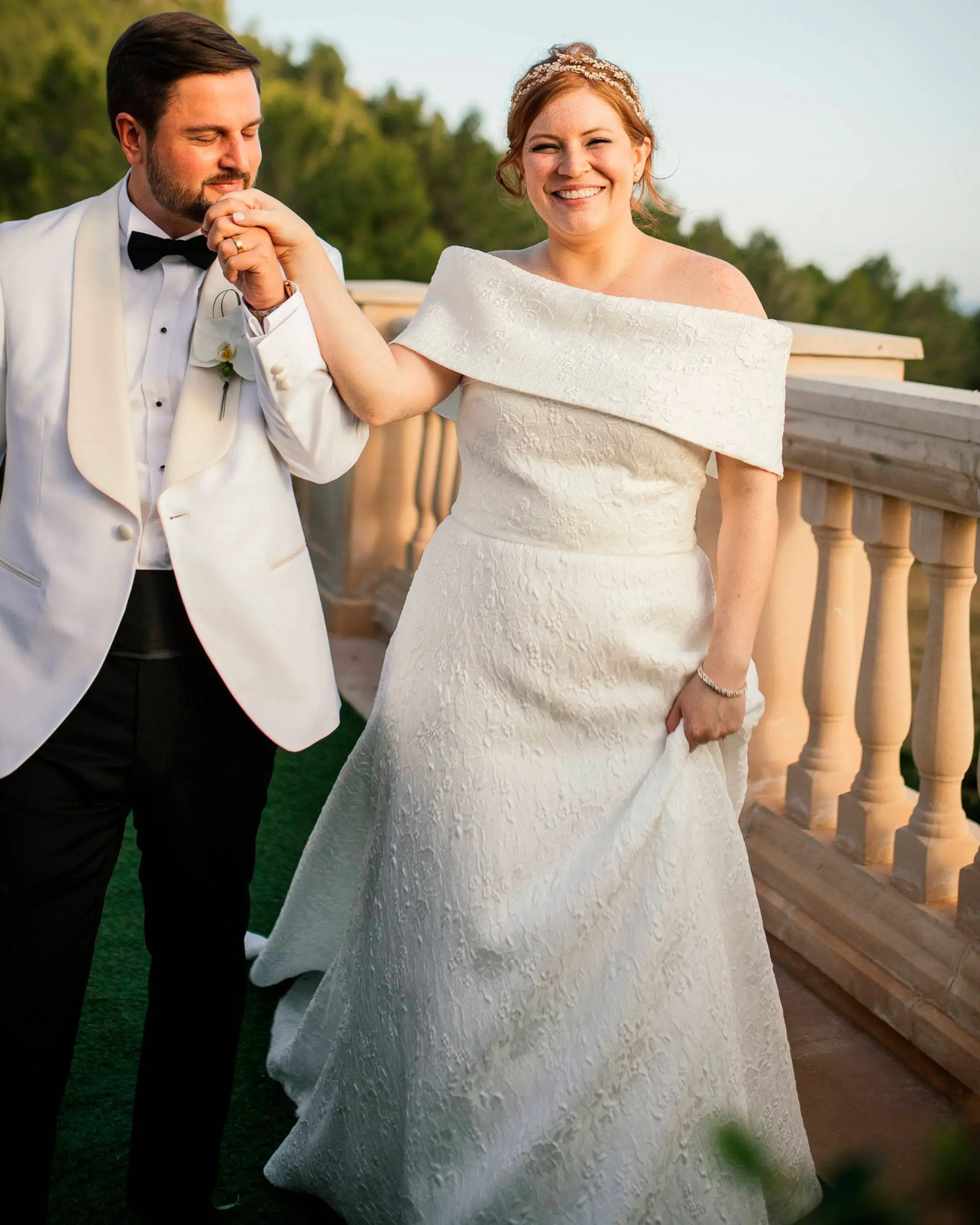 Mau besa la mano de Stephanie, ambos vestidos de novios, en una escena romántica con el hermoso paisaje natural de Mallorca al fondo.