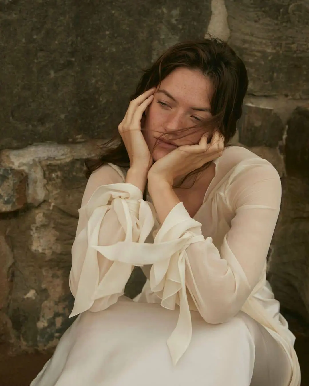 Novia pensativa sentada, luciendo un vestido diseñado por Claudia Llagostera.