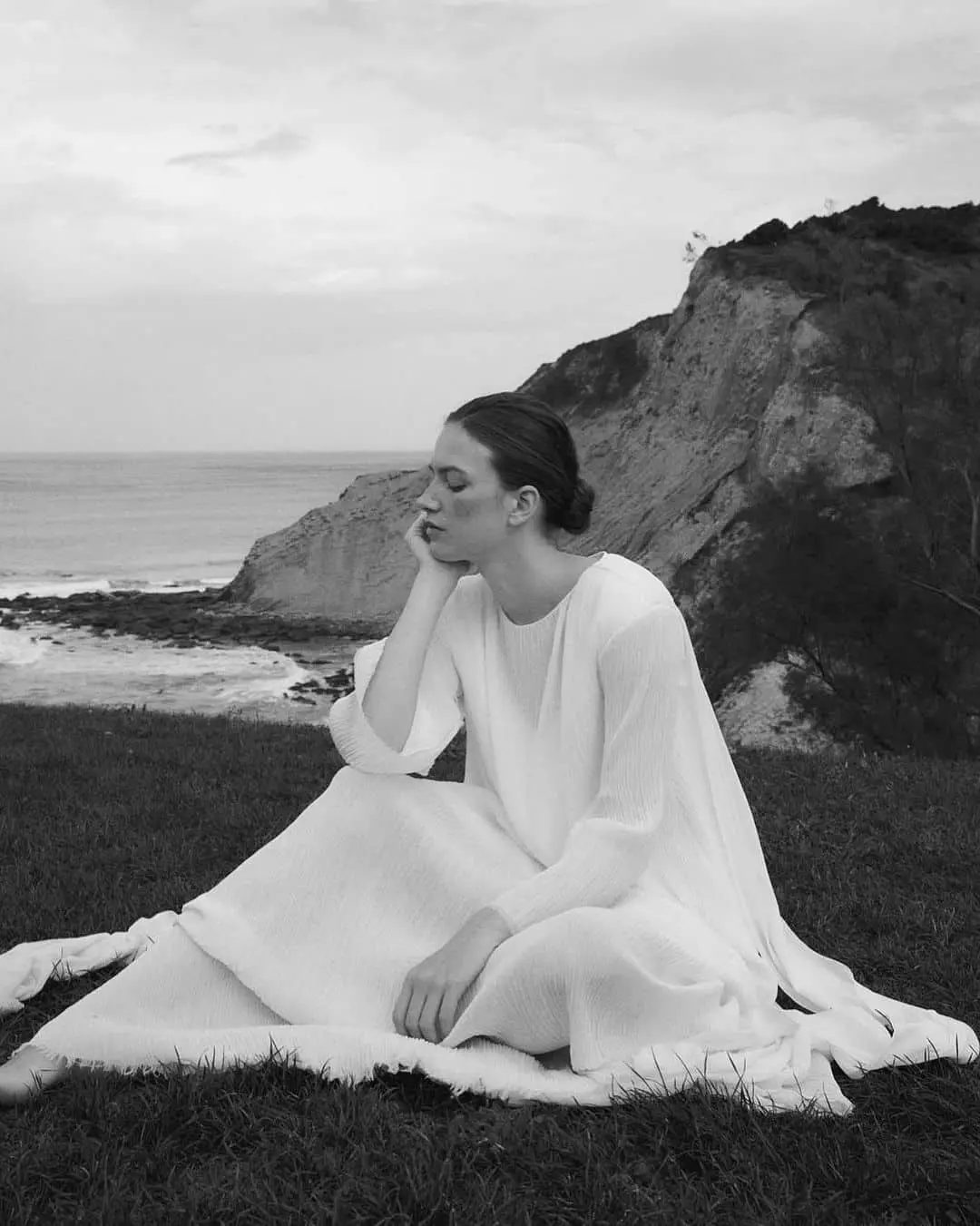 Novia sentada luciendo un vestido de Claudia Llagostera con el mar como telón de fondo.