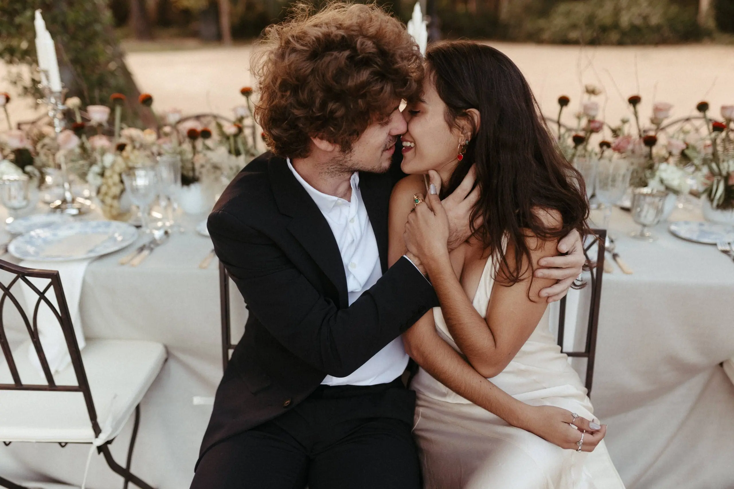 Novios compartiendo un beso sentados en su mesa de bodas diseñada por Bouclé Weddings.
