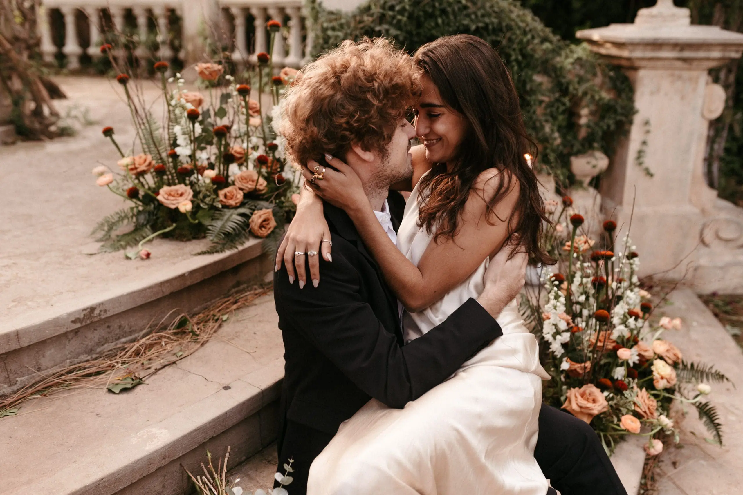 Novios compartiendo un beso con una decoración floral y candelabros de fondo.