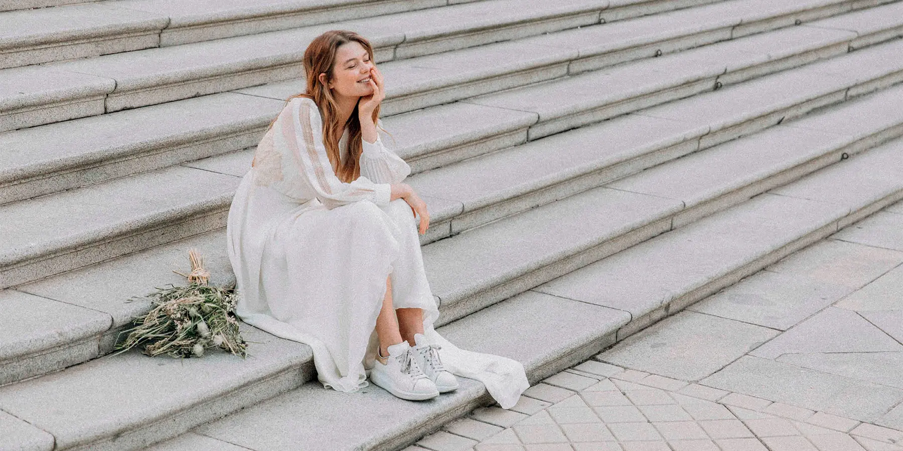 Novia sentada en una escalera con un vestido diseñado por Claudia Llagostera