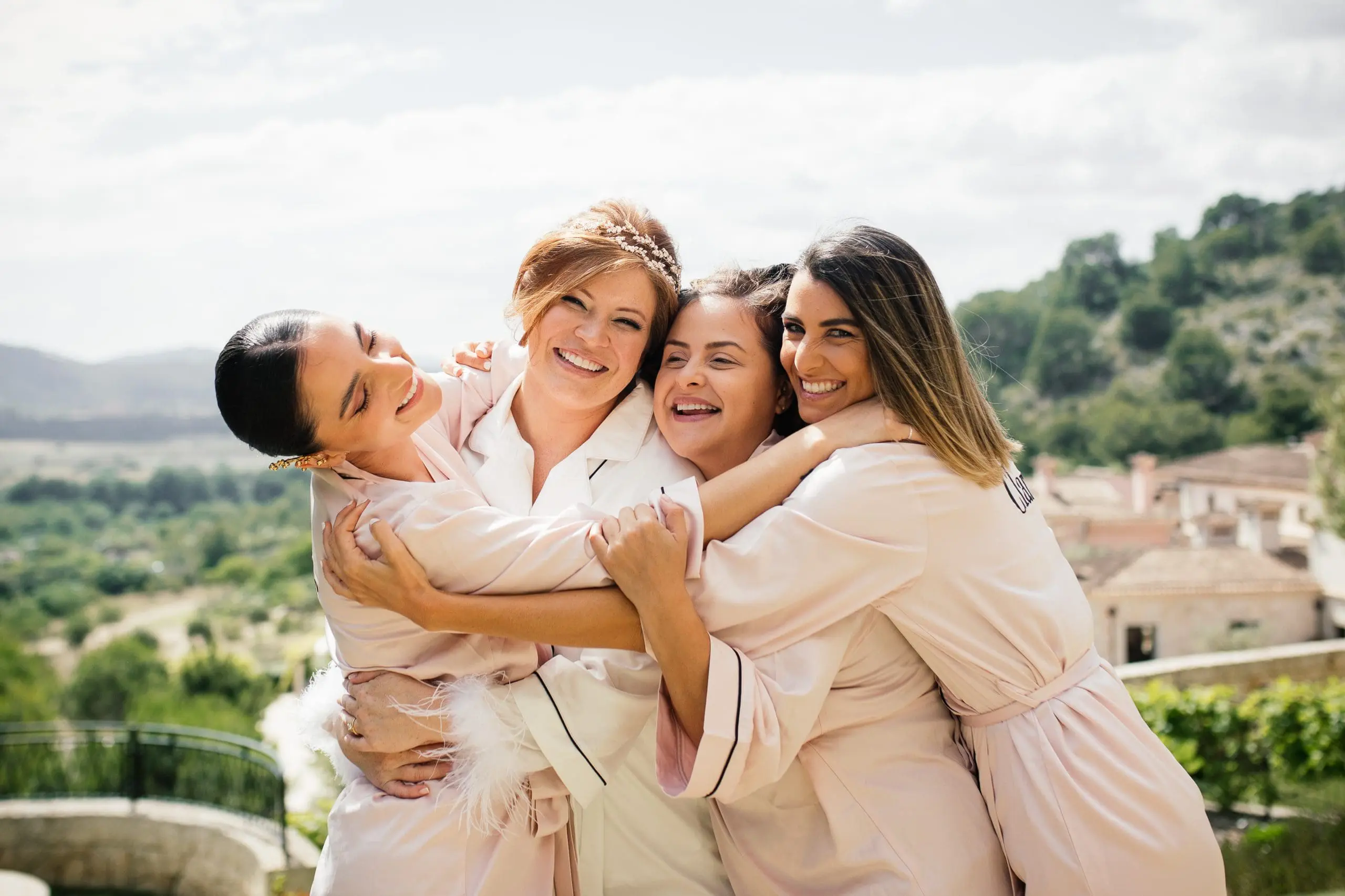 Novia abrazando a sus amigas con las montañas de Mallorca de fondo, antes de vestirse para su boda.