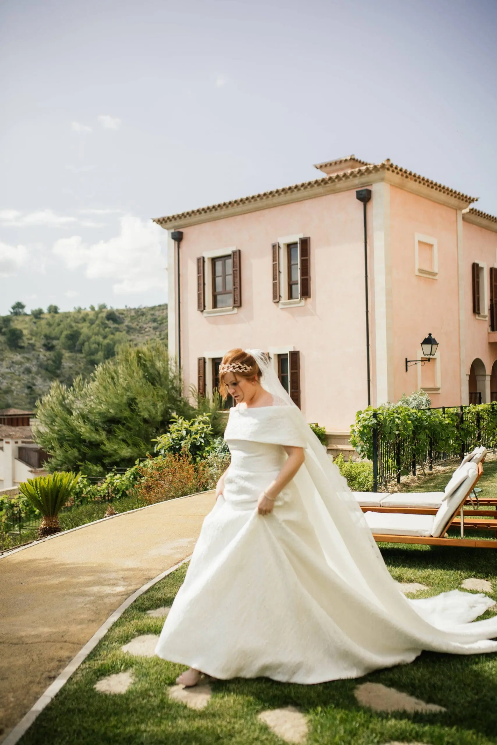 Novia radiante en Mallorca durante el día de su boda, con el lujoso Hotel Cap Vermell al fondo, reflejando la elegancia y la felicidad del día especial.