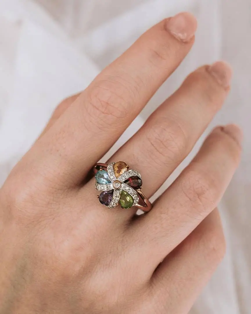 Mano con anillo de compromiso vintage de diseño único engarzado en varios colores, última tendencía de anillos de compromiso para 2025