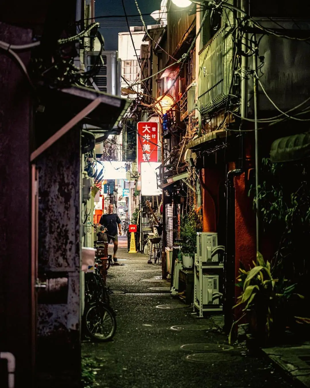 Callejón estrecho en Tokio con cables colgados e iluminación de letreros, ambiente de luna de miel