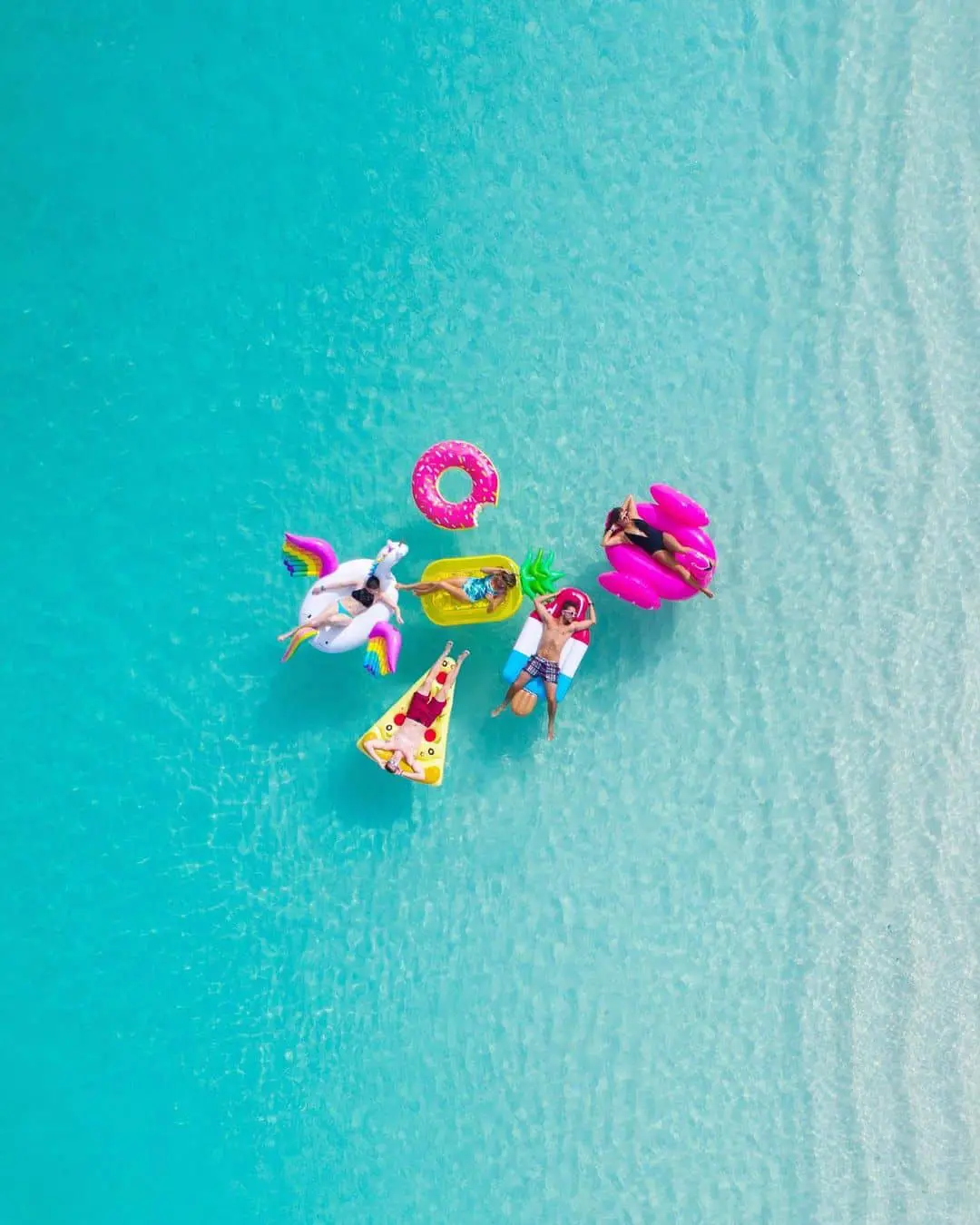 Personas disfrutando del mar en Turcas y Caicos con flotadores de colores durante su luna de miel. Es uno de los mejores destinos para tu luna de miel