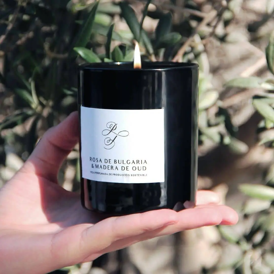 Regalos para invitados: Vela aromática negra encendida sostenida sobre la palma de la mano.