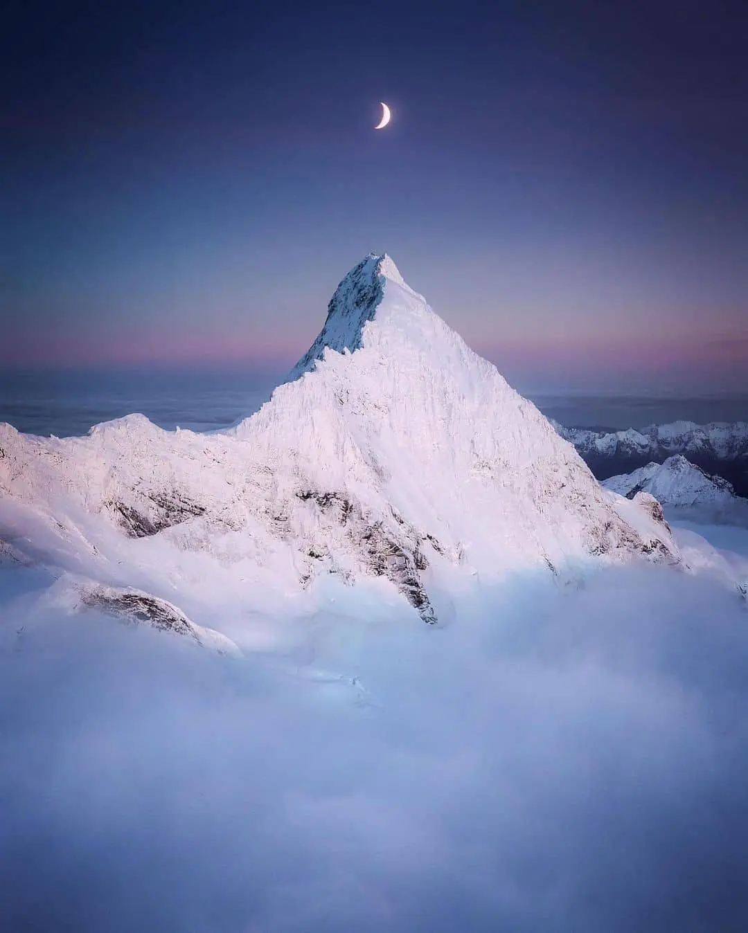 Pico nevado emergiendo sobre las nubes con la luna en el cielo, en Nueva Zelanda, escenario de luna de miel