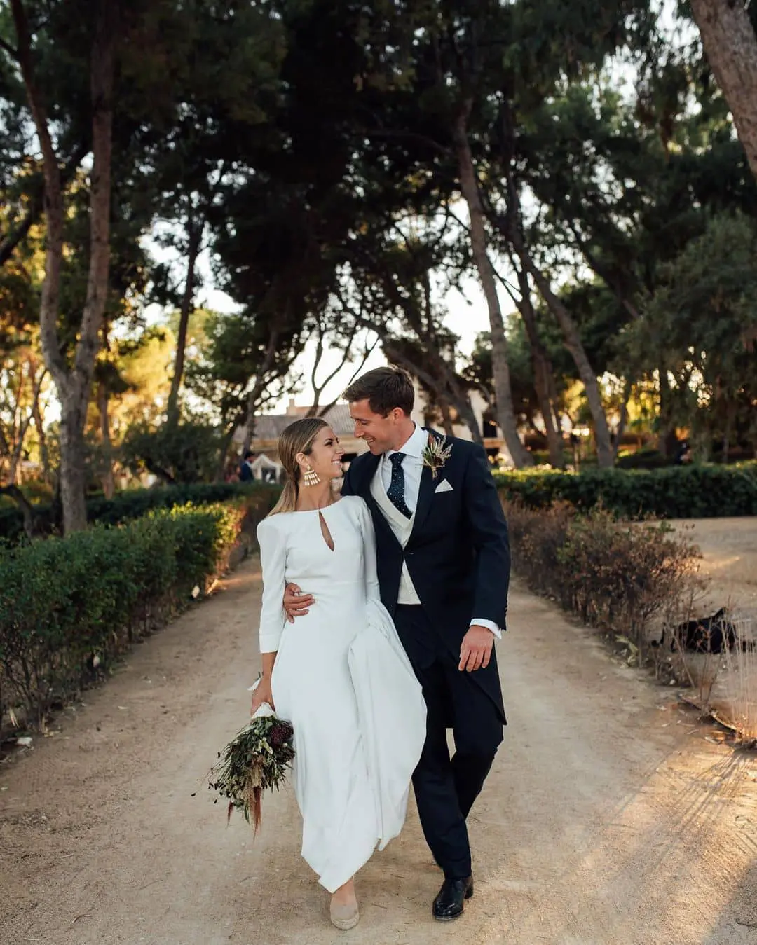 Pareja de novios caminando de la mano con trajes de novio modernos