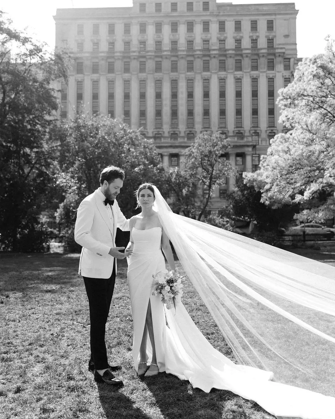 Pareja de novios en atuendos de boda posando para una foto artística en blanco y negro.