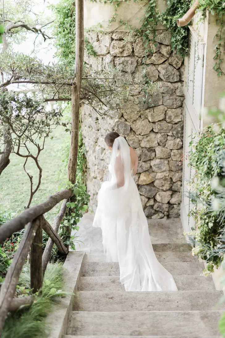 Una novia elegante caminando por los jardines del Hotel Santa Caterina, con el esplendor de la Costa Amalfitana de fondo.