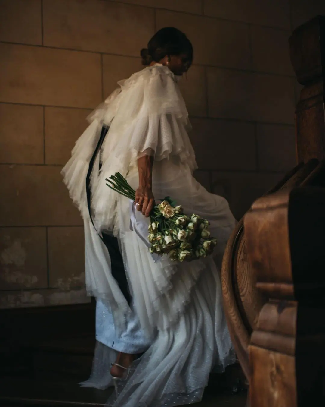 Novia ascendiendo escaleras con ramo y vestido diseñado por Helena Mareque