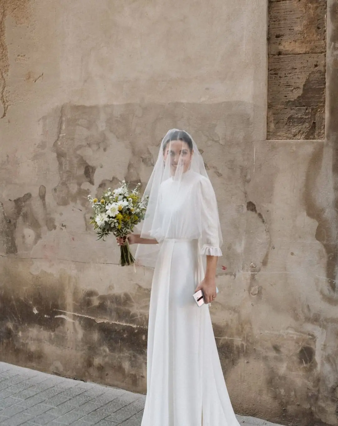 Novia sonriente posando con su elegante ramo de novia tendencia en 2025