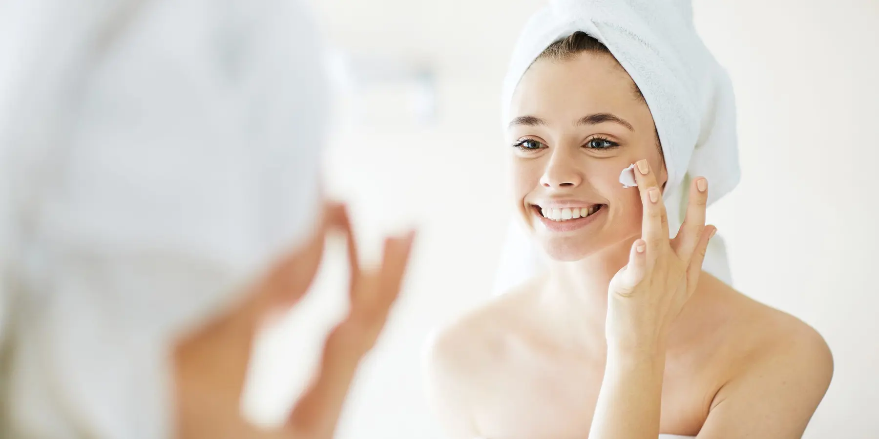Novia aplicando crema facial frente al espejo como parte de su rutina de cuidado de la piel antes de la boda.