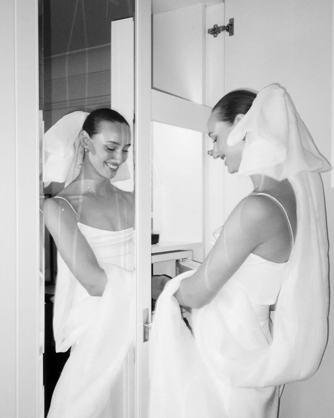 Novia posando frente a un espejo en fotos de boda, sonriendo mientras sostiene su vestido.