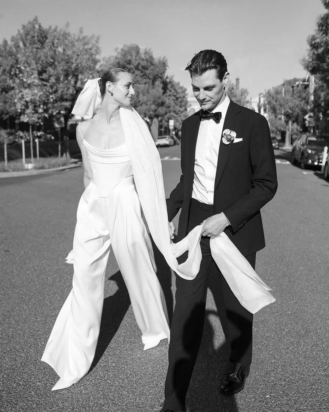 Bride and groom walking hand in hand, posing for wedding photos on the street.