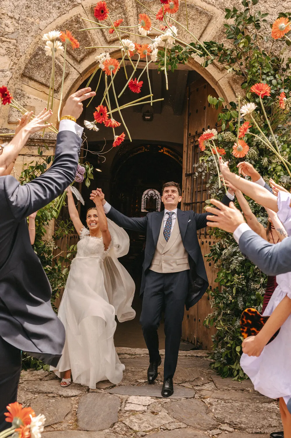 Novios saliendo de una iglesia tras su ceremonia mientras los invitados les lanzan flores de colores.