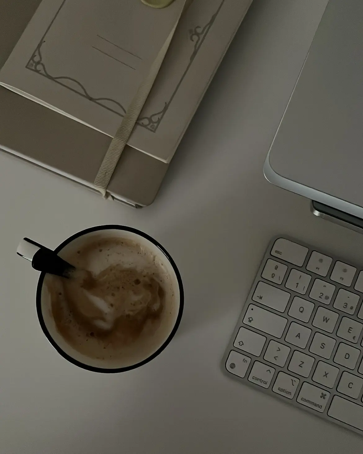 Taza de café con espuma junto a un cuaderno y un teclado sobre un escritorio, parte de una rutina de mañanas productiva.