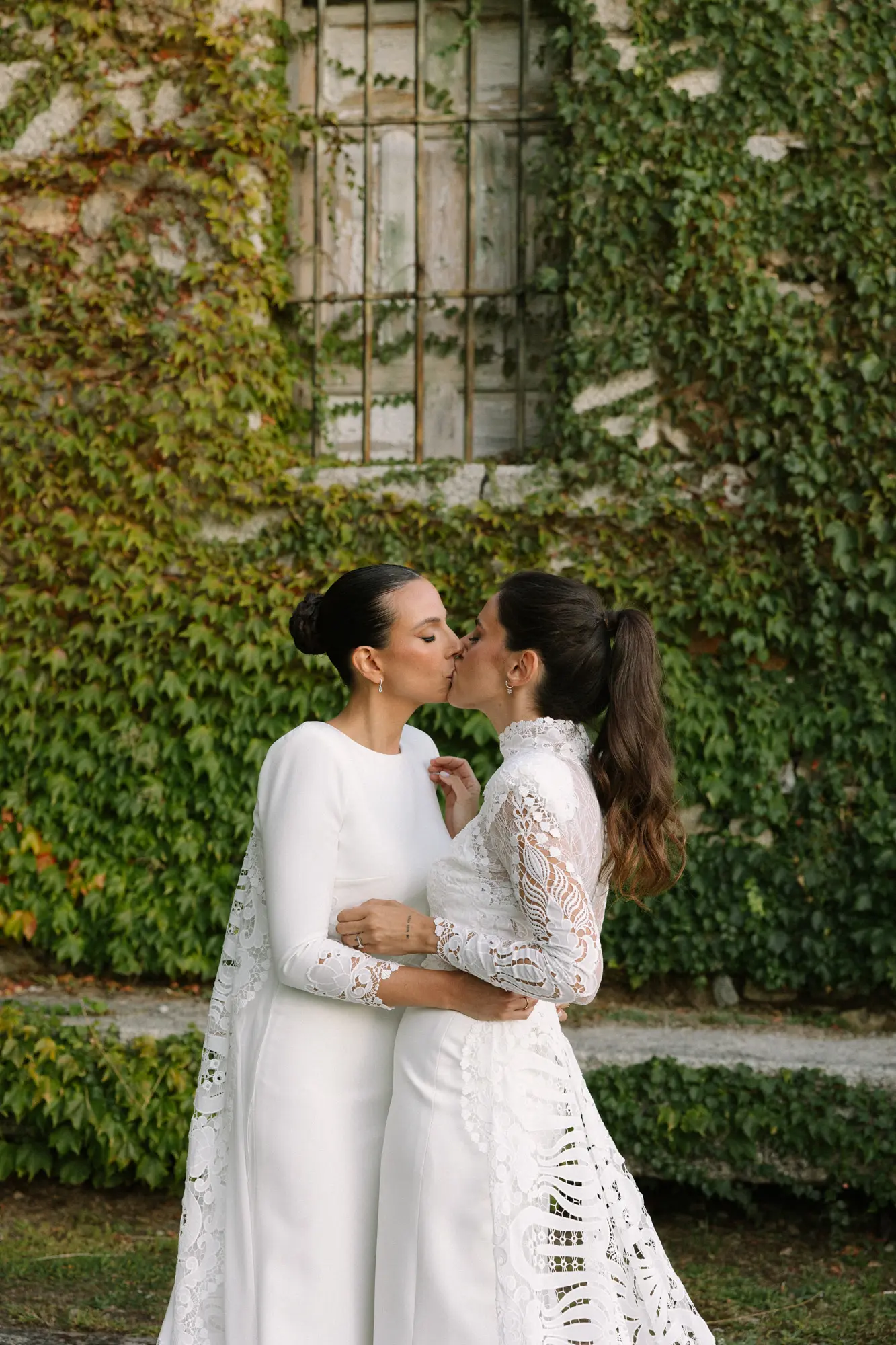 Dos novias besándose frente a una pared cubierta de hiedra