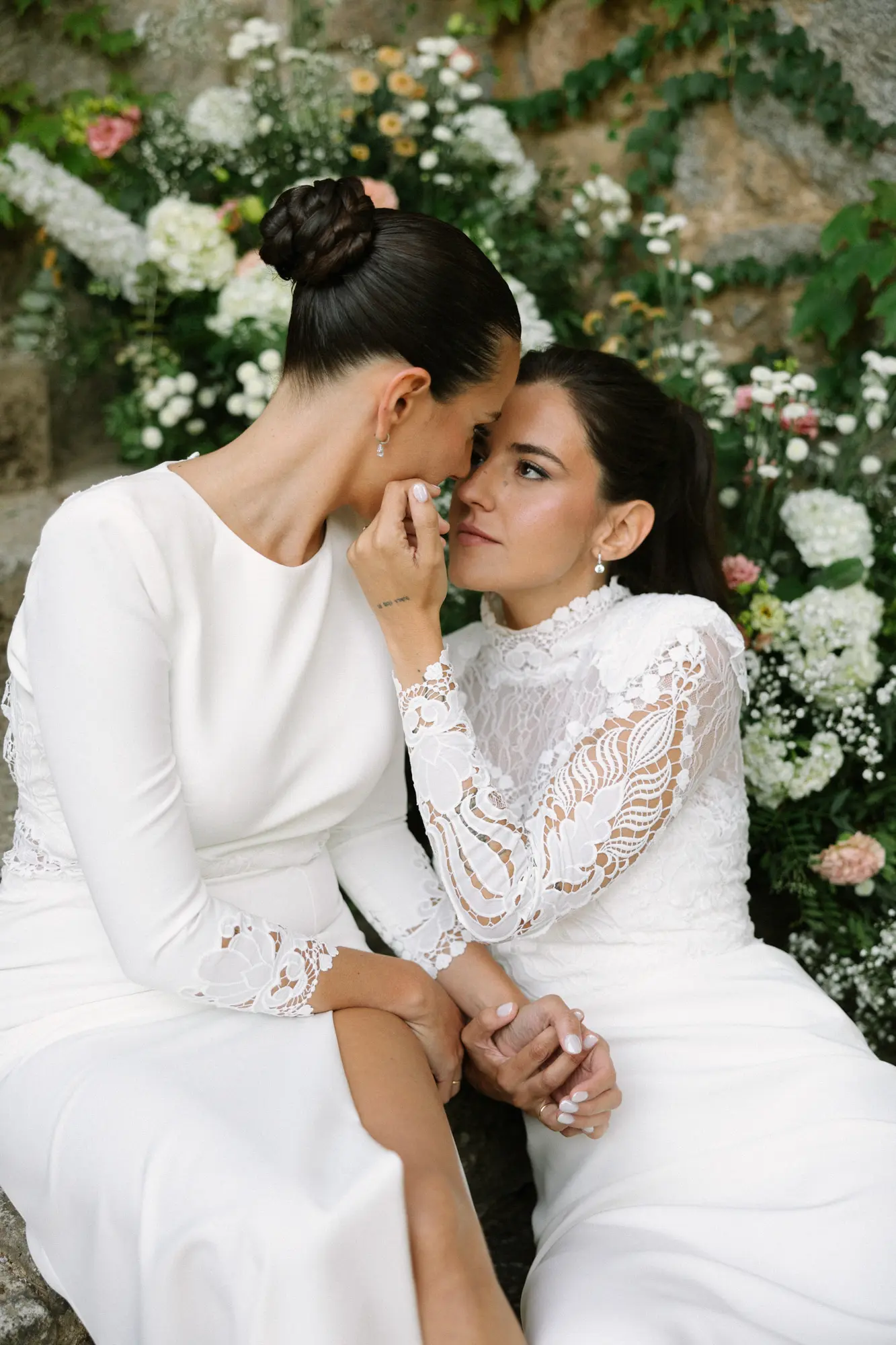 Dos novias compartiendo un momento íntimo frente a un fondo floral