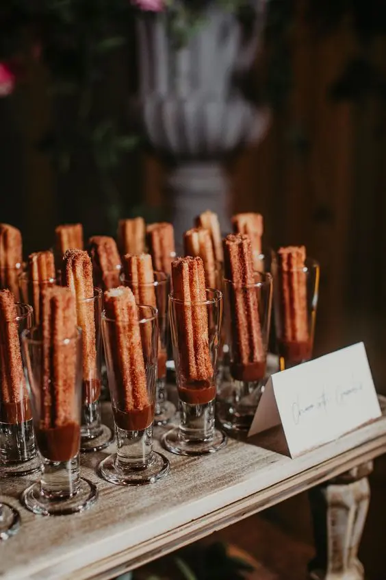 Churros servidos en vasos con chocolate caliente, una recena dulce para bodas.