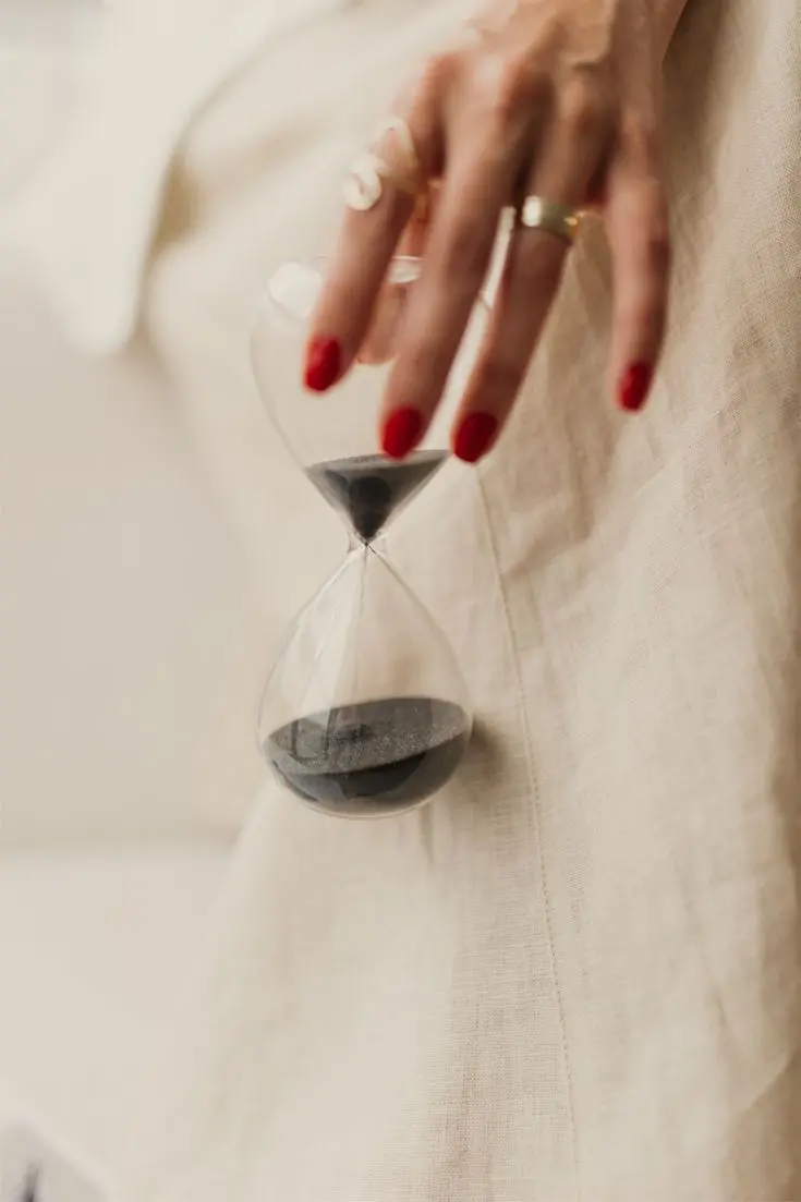 Mano femenina con uñas rojas sujetando un reloj de arena en movimiento.