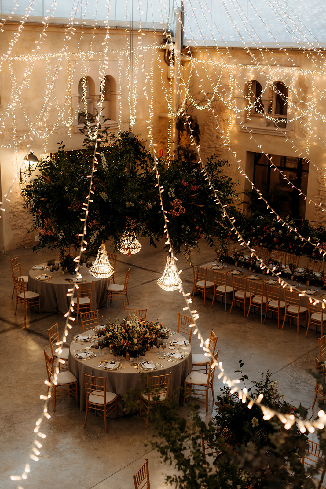 Patio jardín de boda sencillo, elegante y natural con mesas florales y luces colgantes.