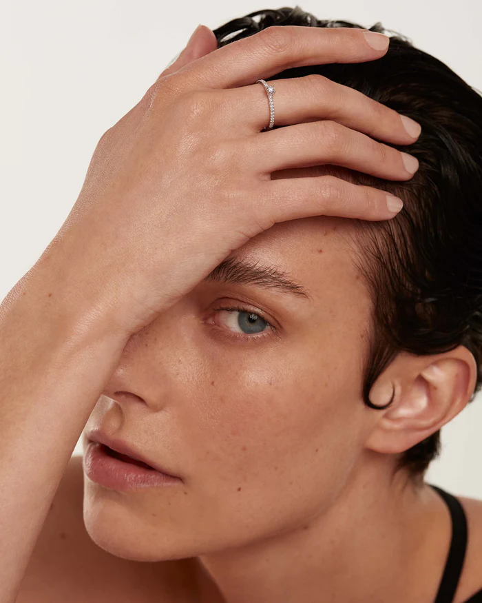 Mujer posando con la mano en la frente mientras lleva un anillo de compromiso sencillo de Pdpaola