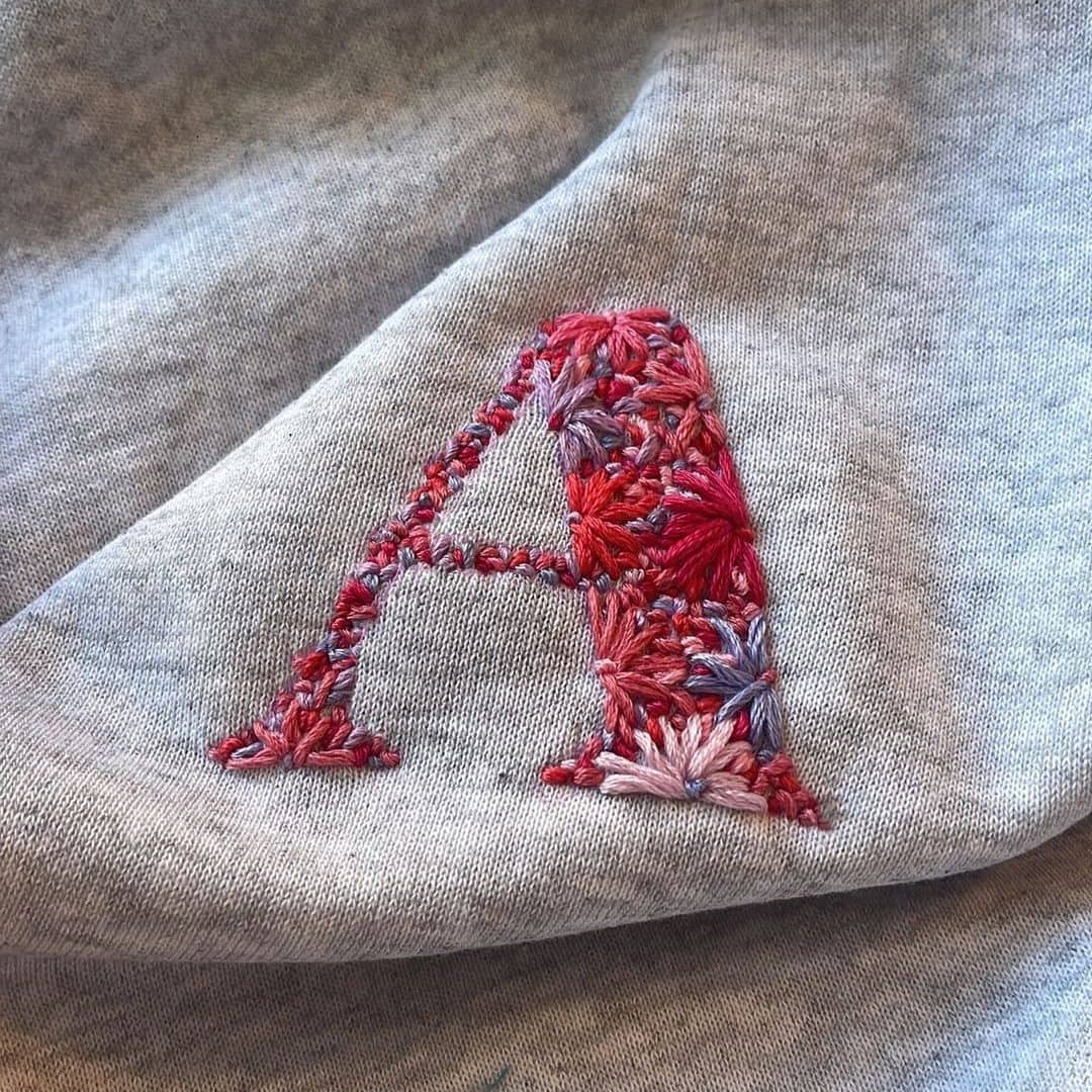 Regalos para invitados: Sudadera gris con bordado personalizado en tonos rojos de la letra 'A' mayúscula.