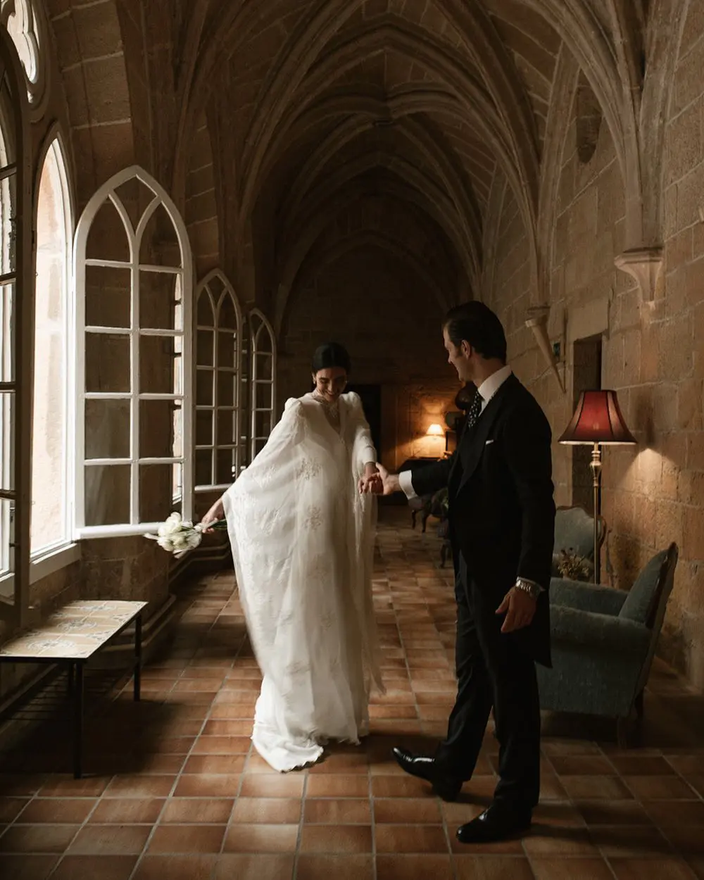 Novios agarrados de la mano en una finca con arcos góticos, celebrando su boda en otoño.
