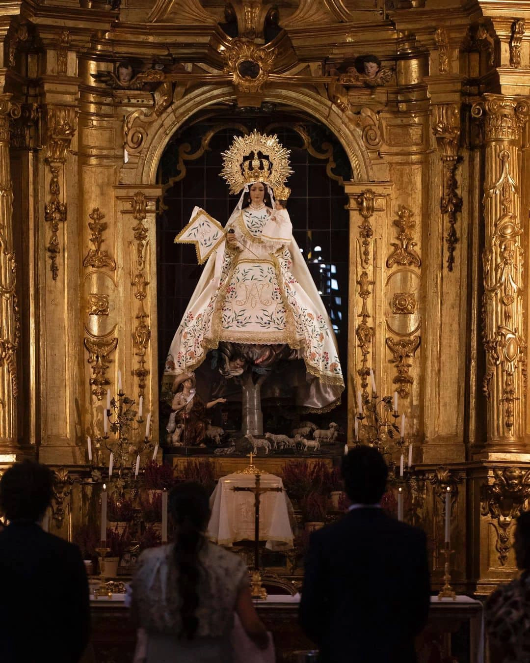 Novios en la ceremonia de su boda en la iglesia, mirando la imagen de la Virgen María durante el rito de la velación - Bouclé Weddings