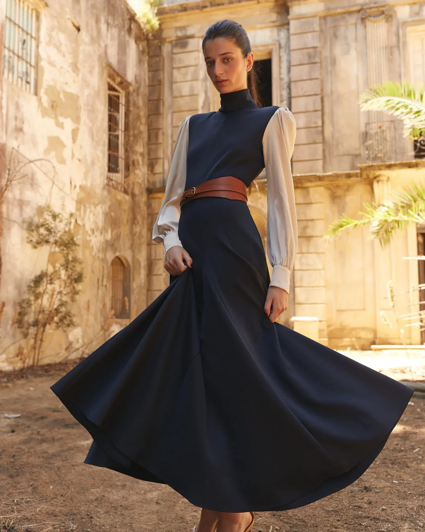 La modelo muestra el Vestido Aidan Marino de The IQ Collection, de frente, dándole vuelo a la falda de neopreno azul marino, destacando su diseño dinámico y elegante.