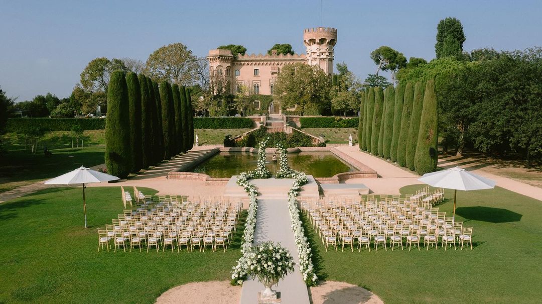 Ceremonia de boda al aire libre en los jardines del Castell de Sant Marçal, con vistas a la imponente arquitectura del castillo.