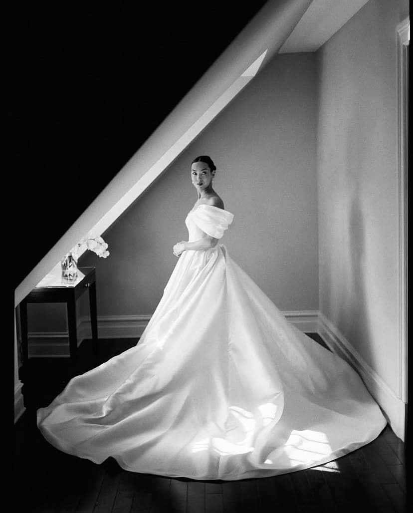 Novia con vestido de cola larga en un rincón iluminado, destacando un diseño clásico y sofisticado.