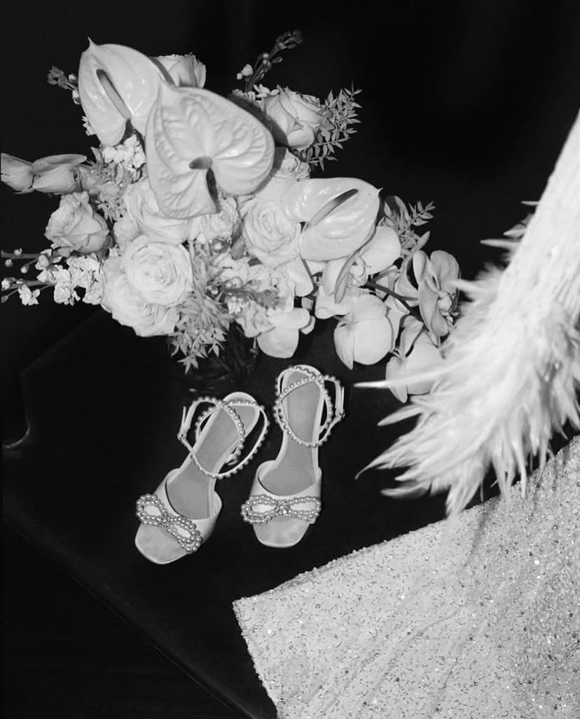 Zapatos decorados con perlas junto a un ramo de flores blancas y un vestido brillante, detalles elegantes para una boda.