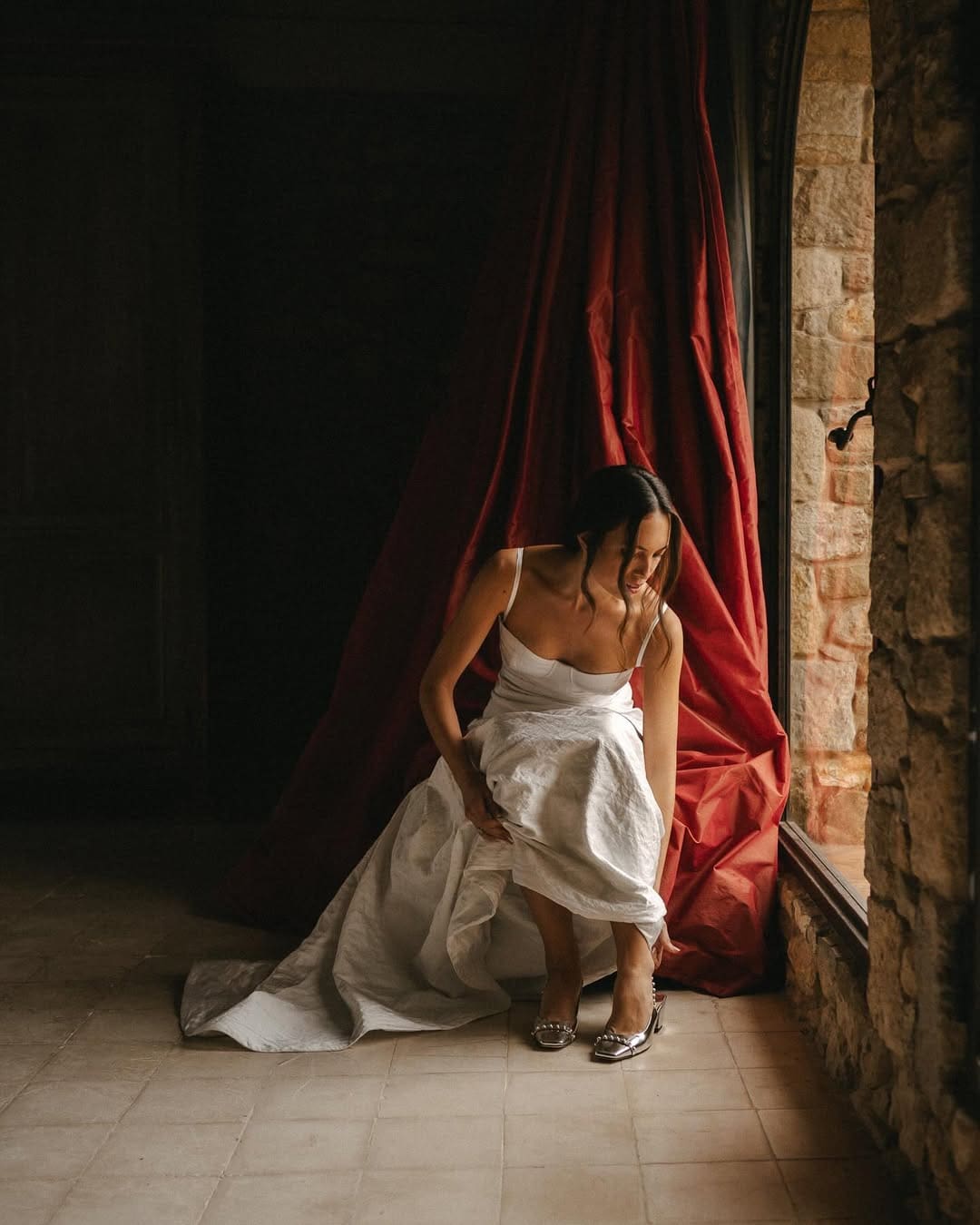 Novia arreglándose los zapatos en una habitación con luz tenue.