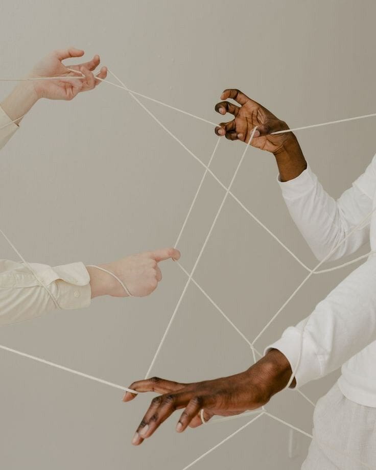 Manos de varias personas entrelazadas por hilos blancos, simbolizando conexiones y tensiones.